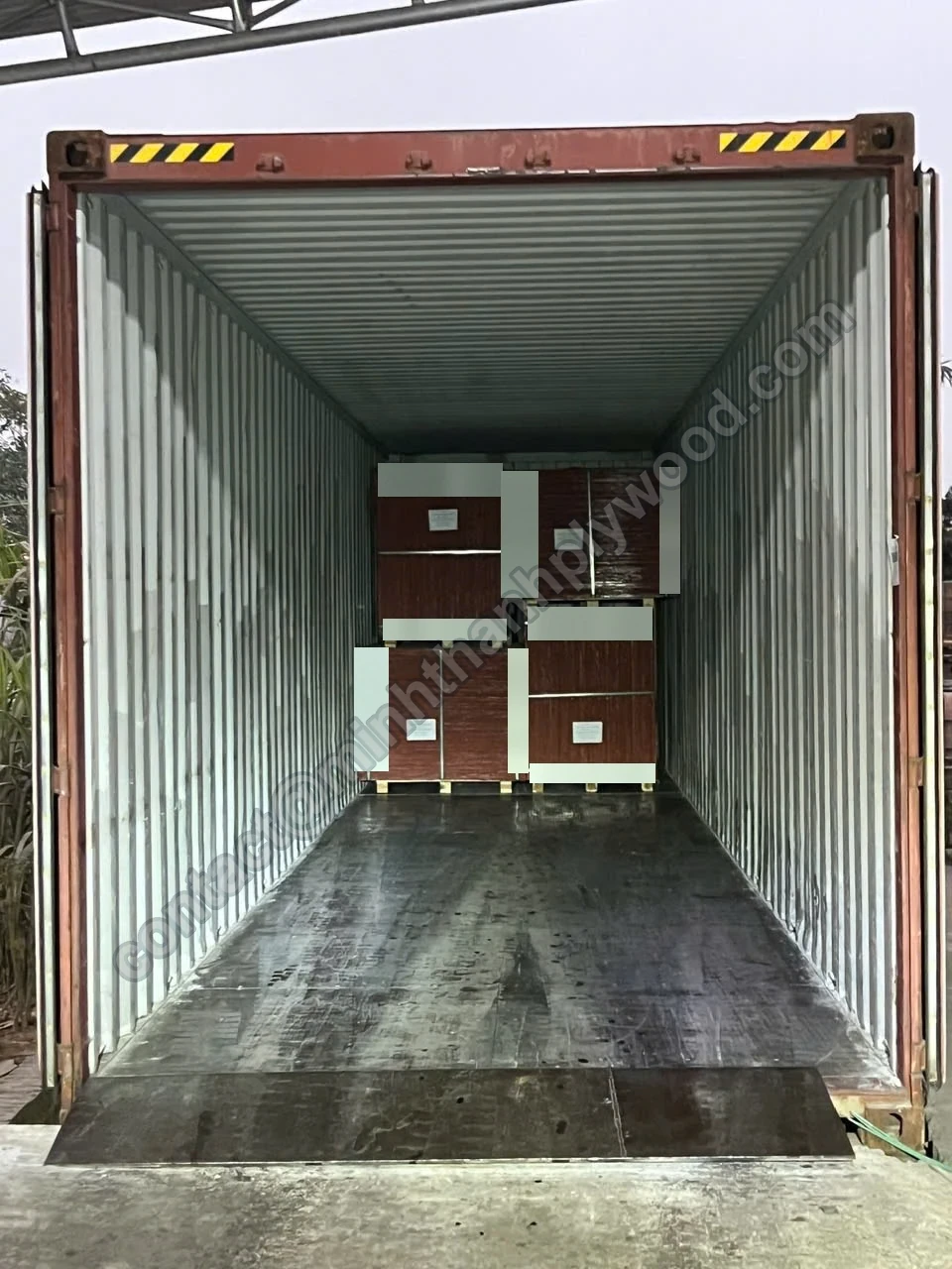 Four strapped film-faced plywood packs stacked two-high at the front wall of an open container