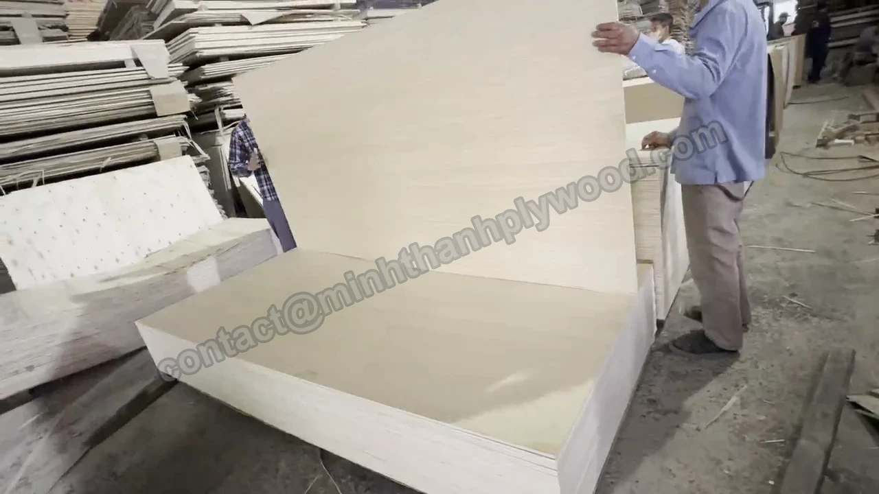 Worker holding a broad pale furniture plywood sheet beside packs