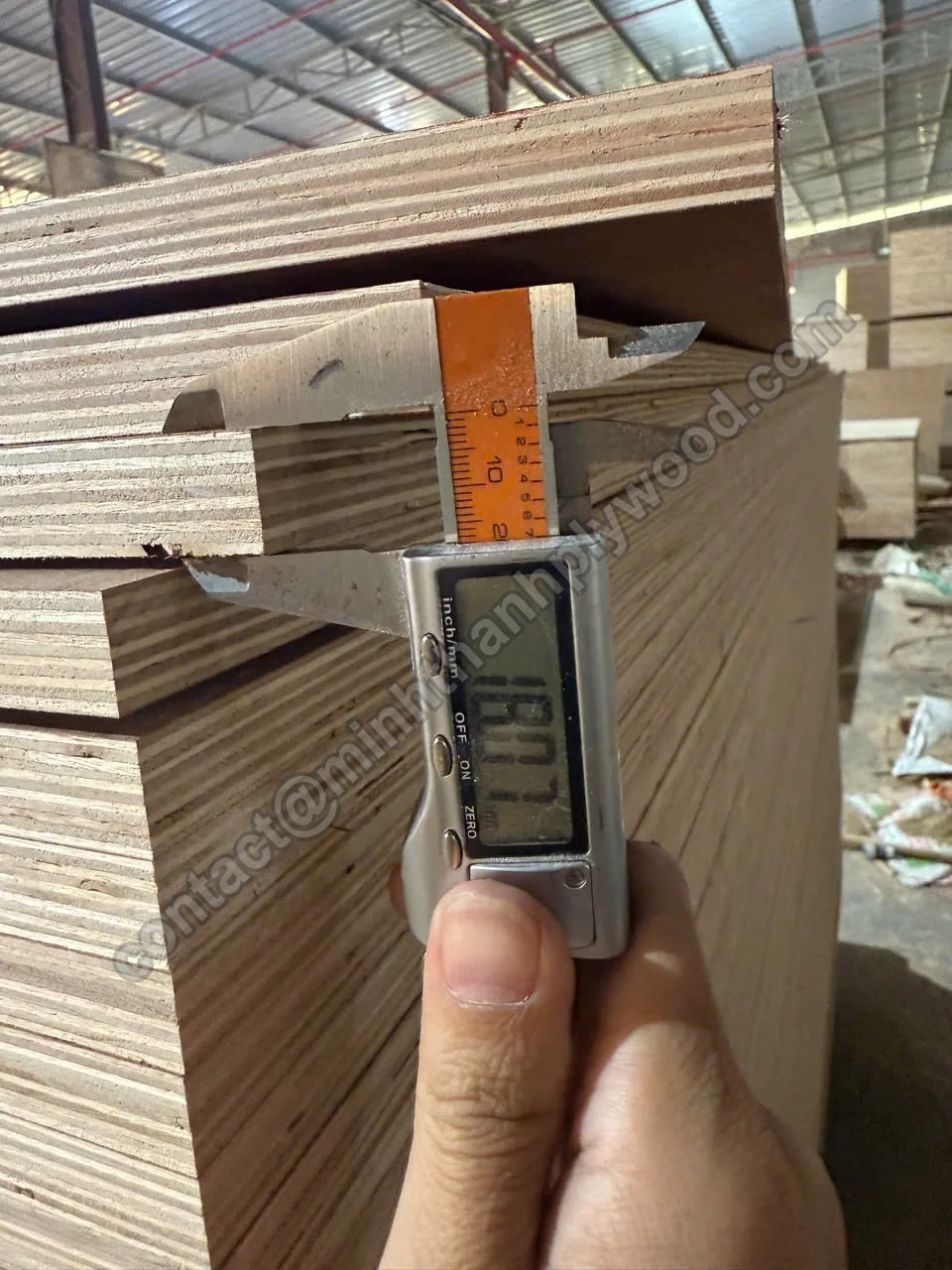 Digitale schuifmaat aan de rand van een multiplexplaat van 18 mm op een stapel, display toont 18,01