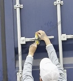 Hænder monterer en gul boltforsegling gennem containerdørens låsehåndtag