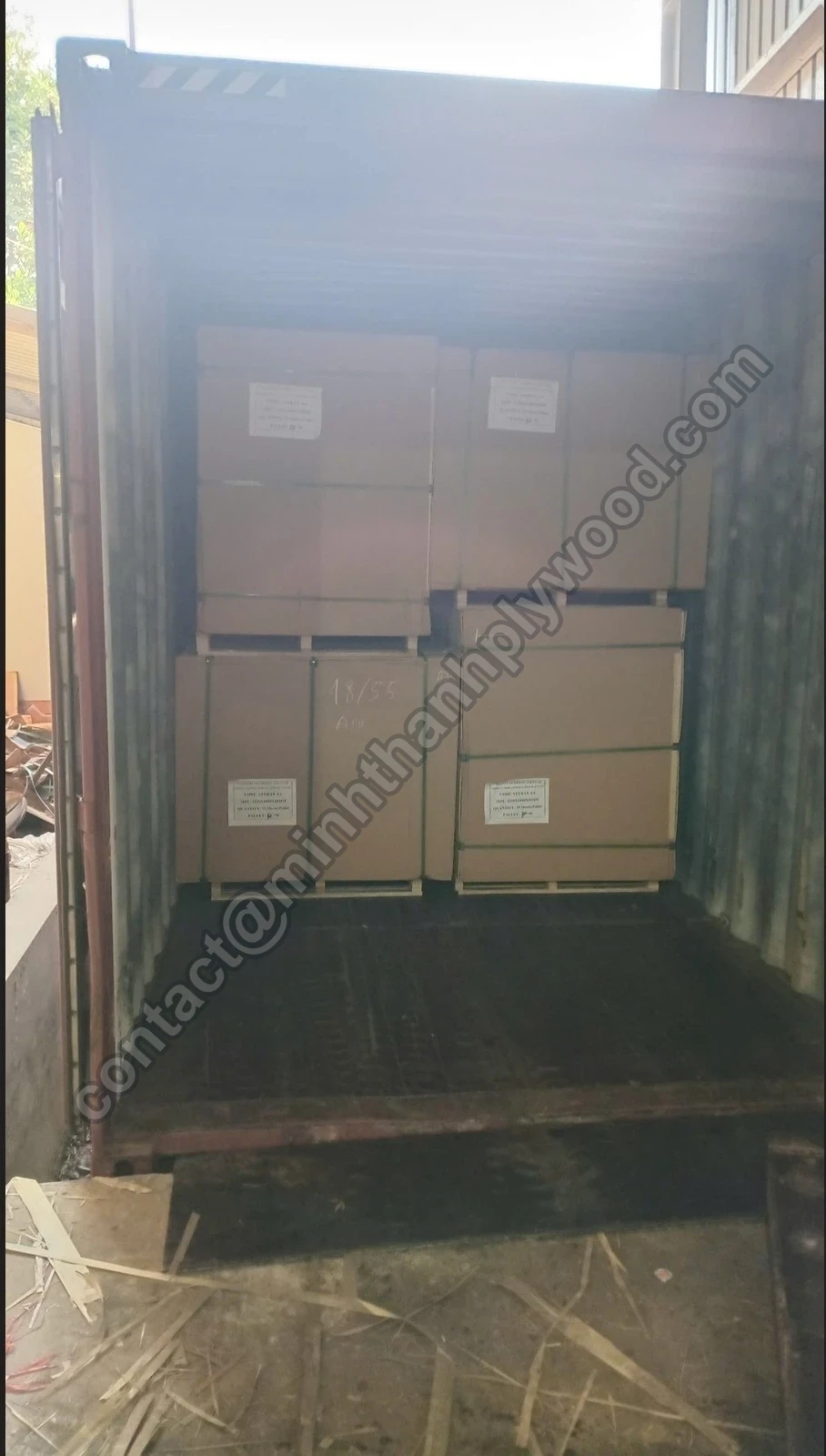 Cardboard-wrapped plywood packs stacked two-high against the end wall of a container