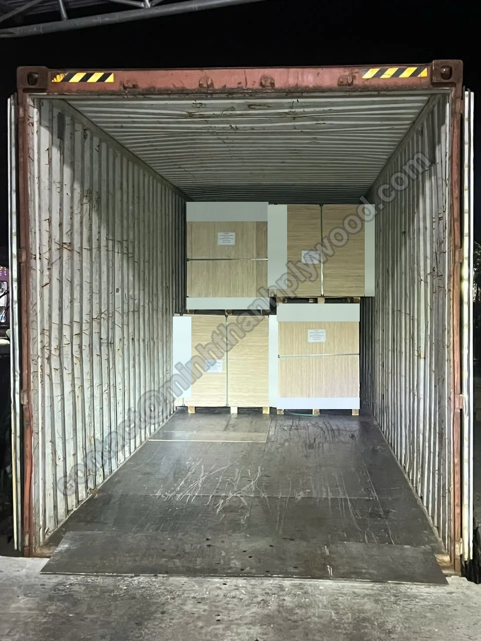 Plywood container loading in progress: four natural-face plywood packs two-high at the front wall of an empty container