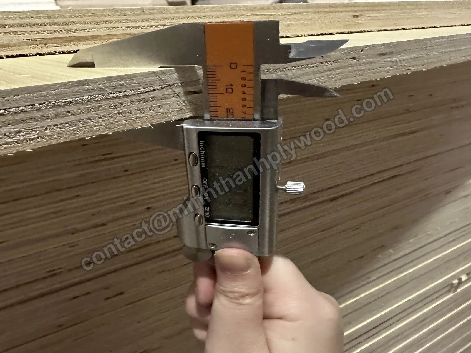 Digital caliper measuring the thickness of a finished plywood panel at the edge of a pack