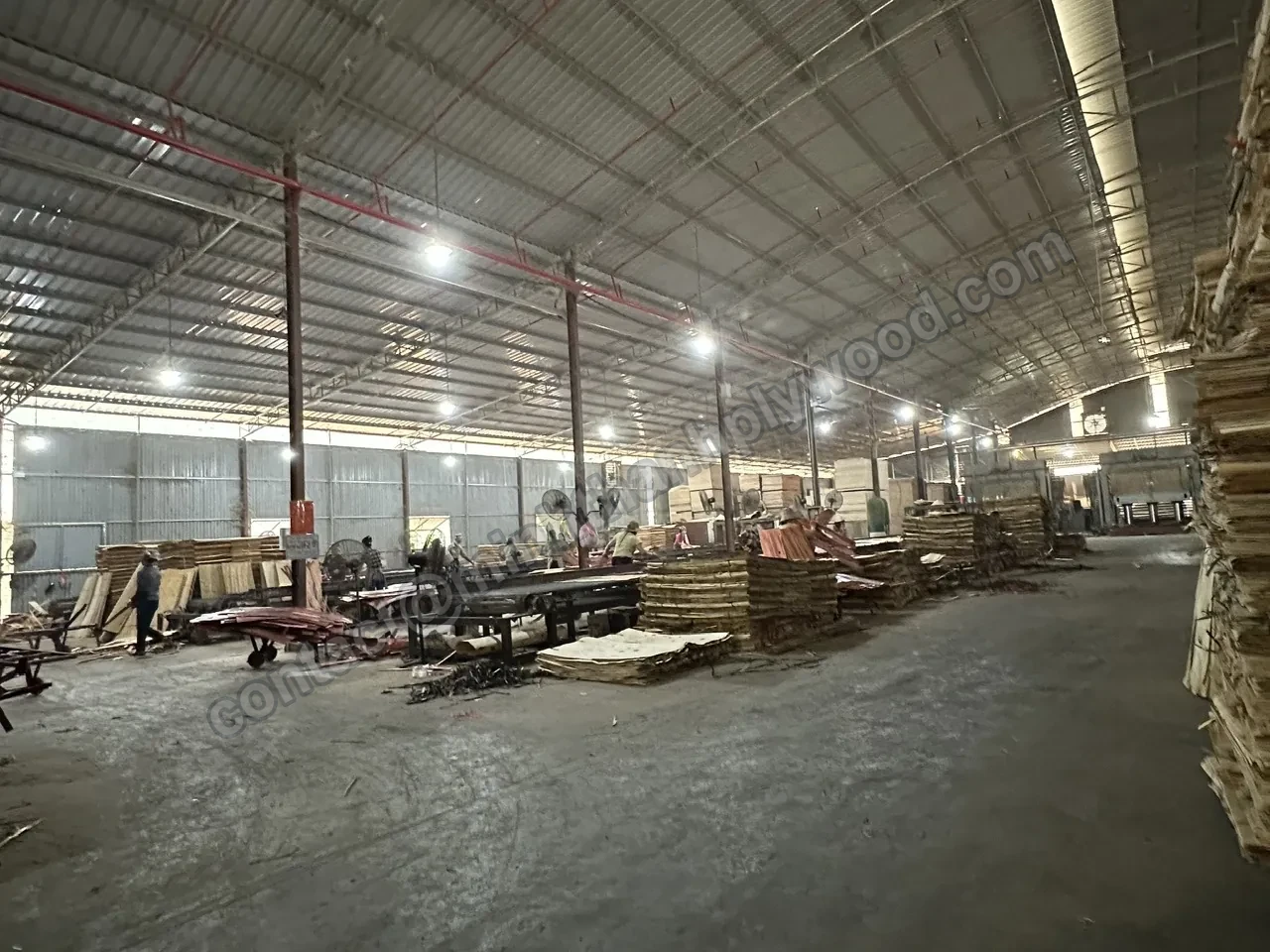 Plywood production hall with veneer stacks and lay-up tables under a high steel roof