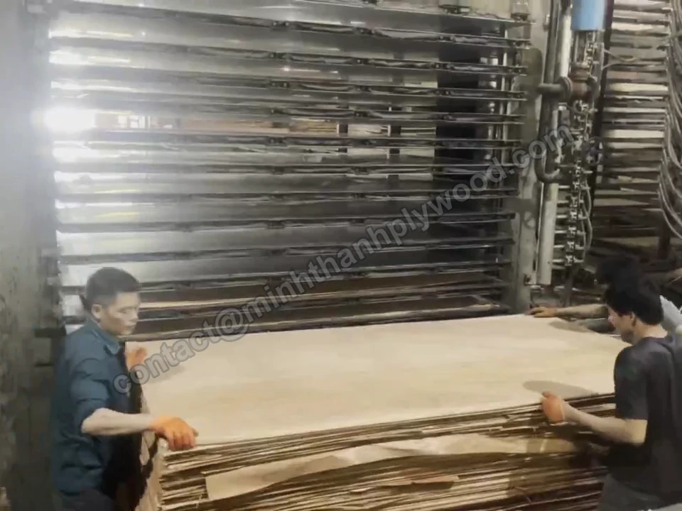 Two workers loading laid-up plywood panels into a multi-opening hot press