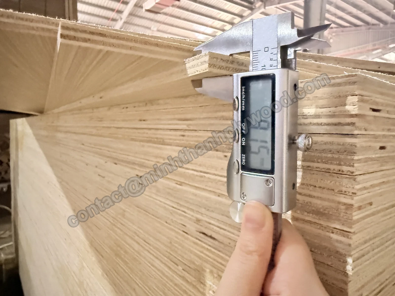Plywood quality control: digital caliper measuring a 9 mm panel at the edge of a stack