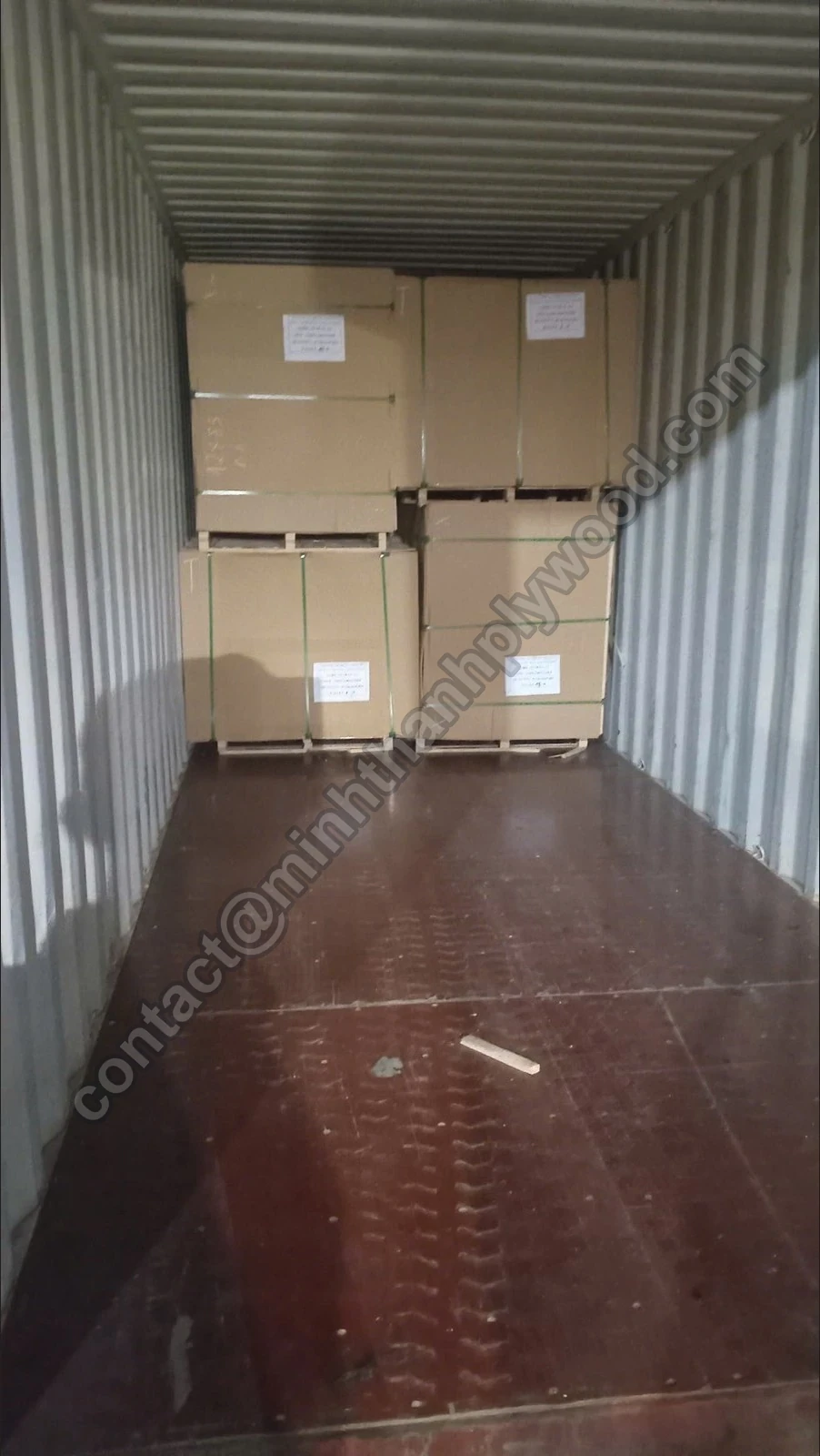 Exportní balíky překližky zabalené v kartonu a stažené páskou, naskládané ve dvou vrstvách na konci kontejneru