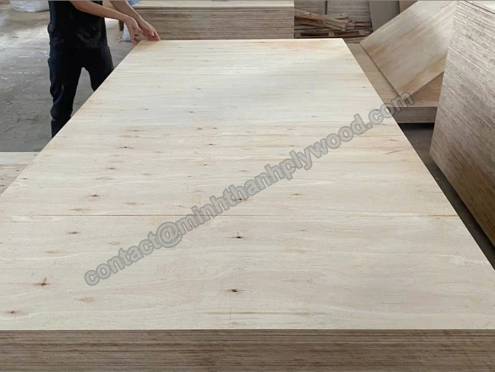 Unfaced pressed plywood board lifted onto a stack, showing the whole sheet and its layered edge